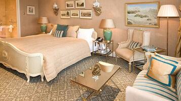 A hotel room with a large bed, a sitting area with a sofa and armchair, a small table, and a bathroom visible through an open door.
