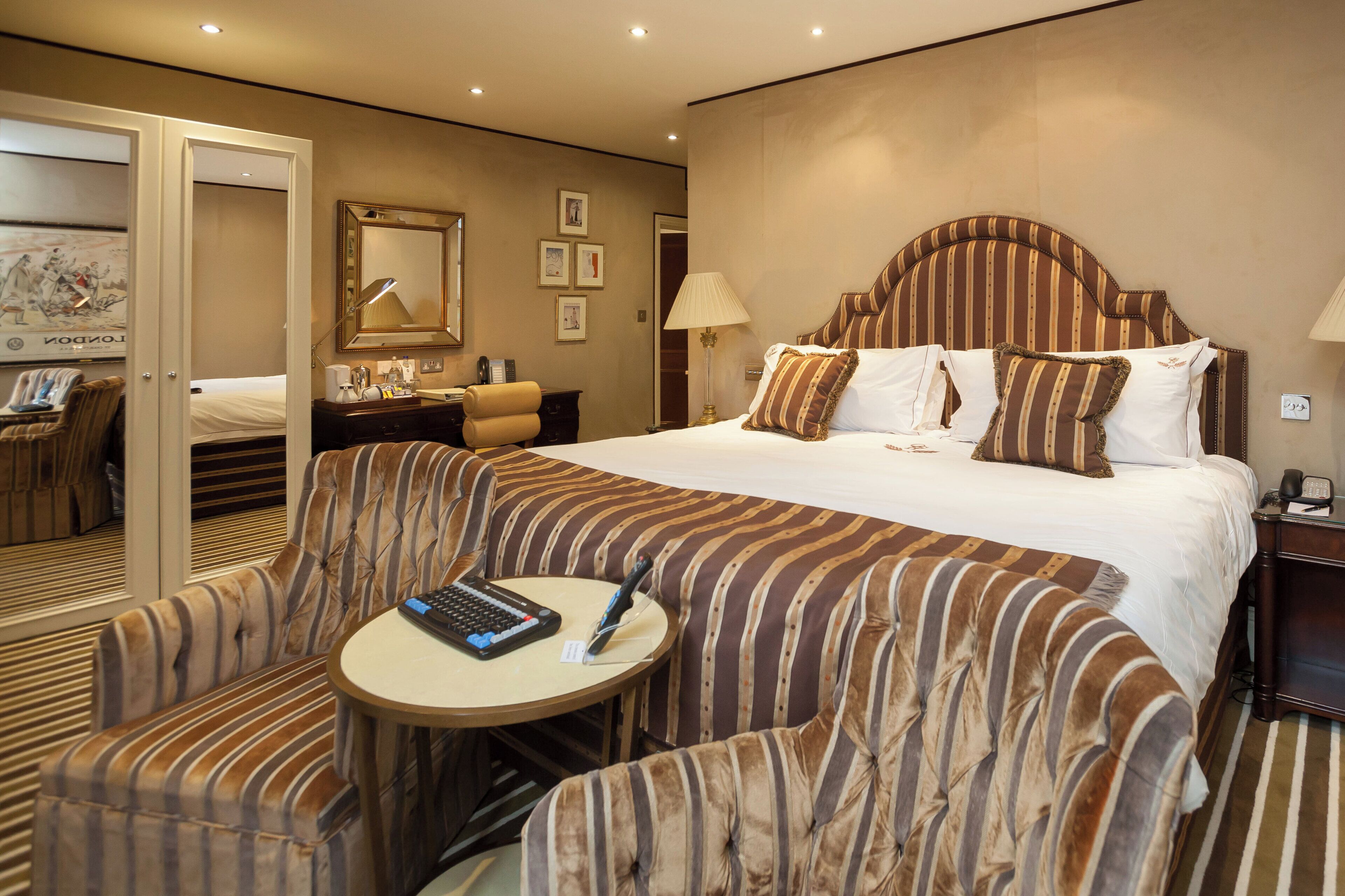 Una habitación de hotel con una cama grande, asientos tapizados a rayas, una mesita redonda con una computadora portátil y un escritorio con una lámpara.