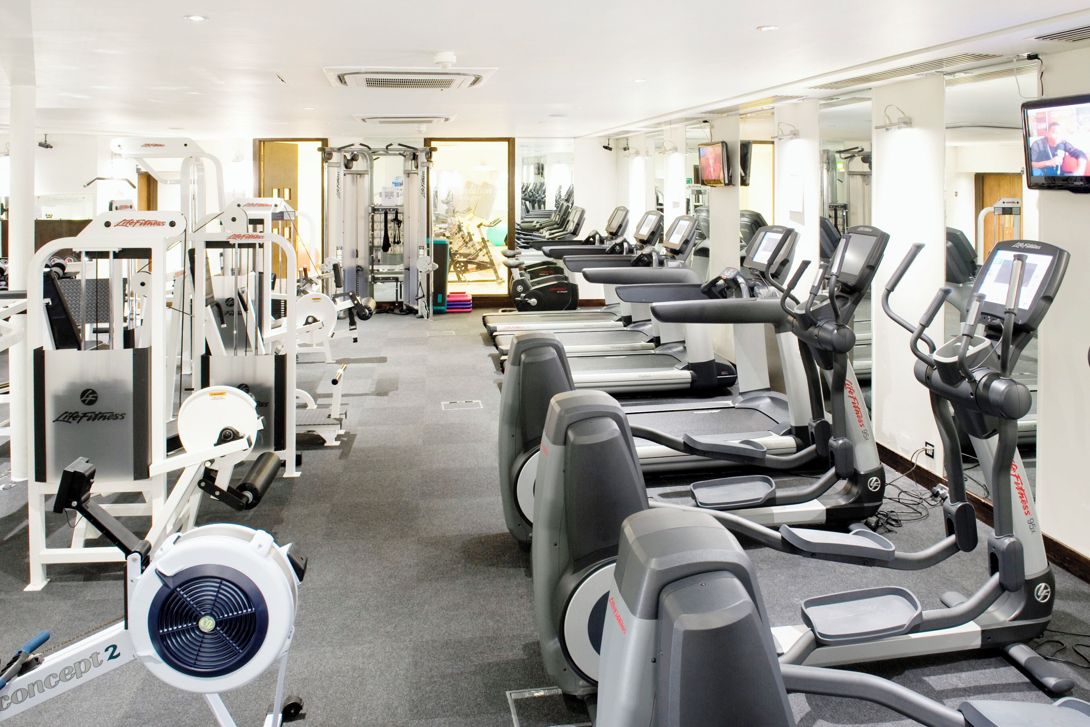 Un gimnasio con cintas de correr, máquinas de pesas y un ventilador.