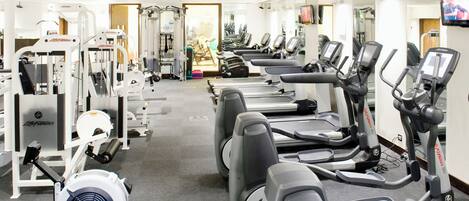 Un gimnasio con cintas de correr, máquinas de pesas y un ventilador.
