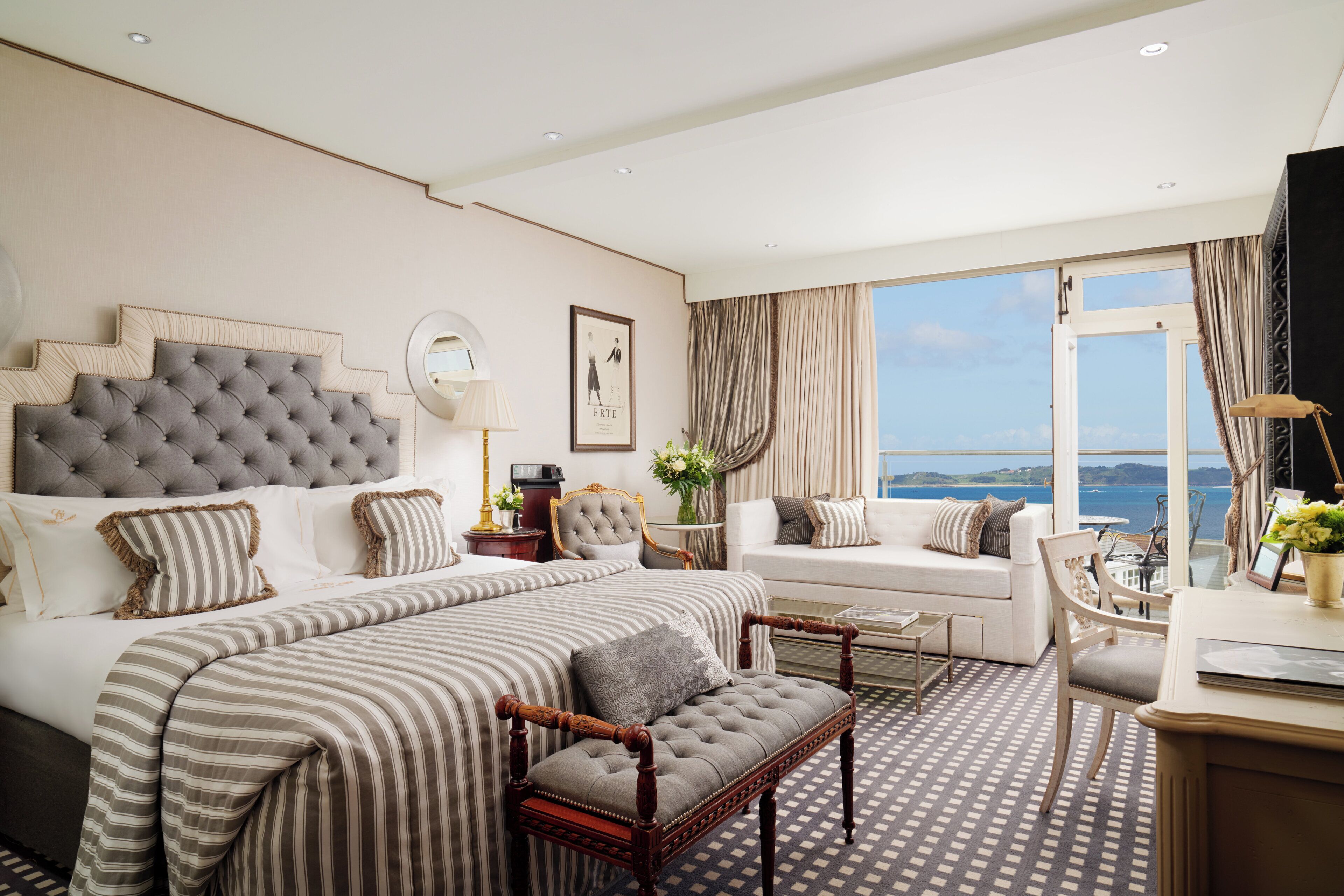 A hotel room with a large bed, a sofa, a desk, and a view of the sea.