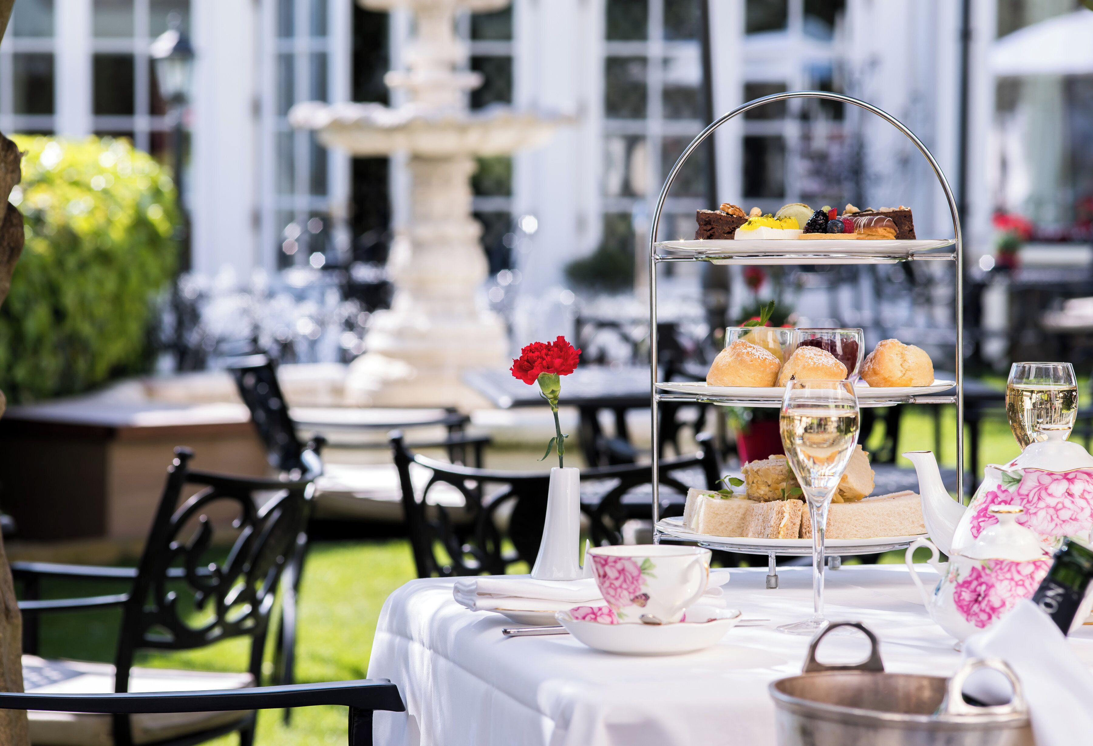 An outdoor dining area with a tiered dessert tray, a teapot, and a vase with a red flower.