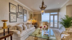 A spacious living room with a large glass coffee table, a white sofa, and a view of the sea through large windows.