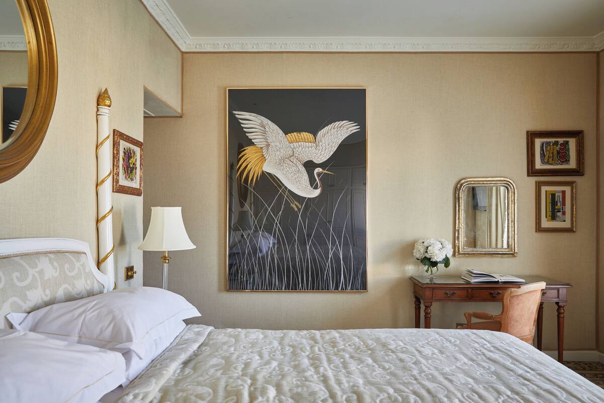 A hotel room with a large bed, a desk with a chair, a mirror, and artwork on the wall.