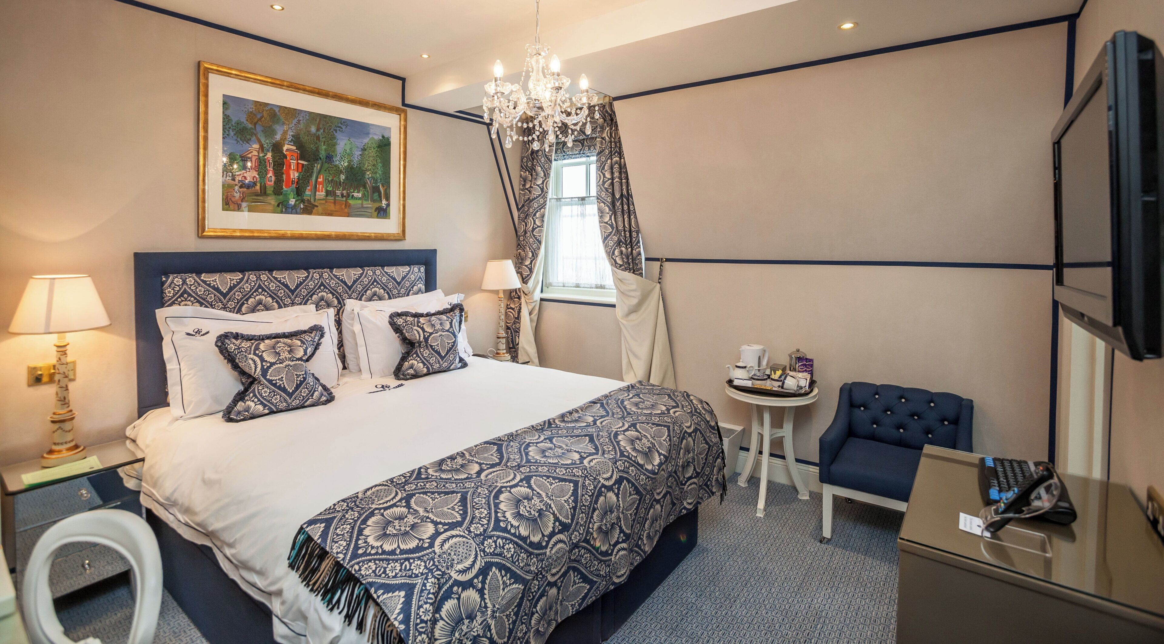 Ein Hotelzimmer mit einem großen Bett, einem kleinen Tisch mit Stuhl, einem Fernseher und einem Bild an der Wand.