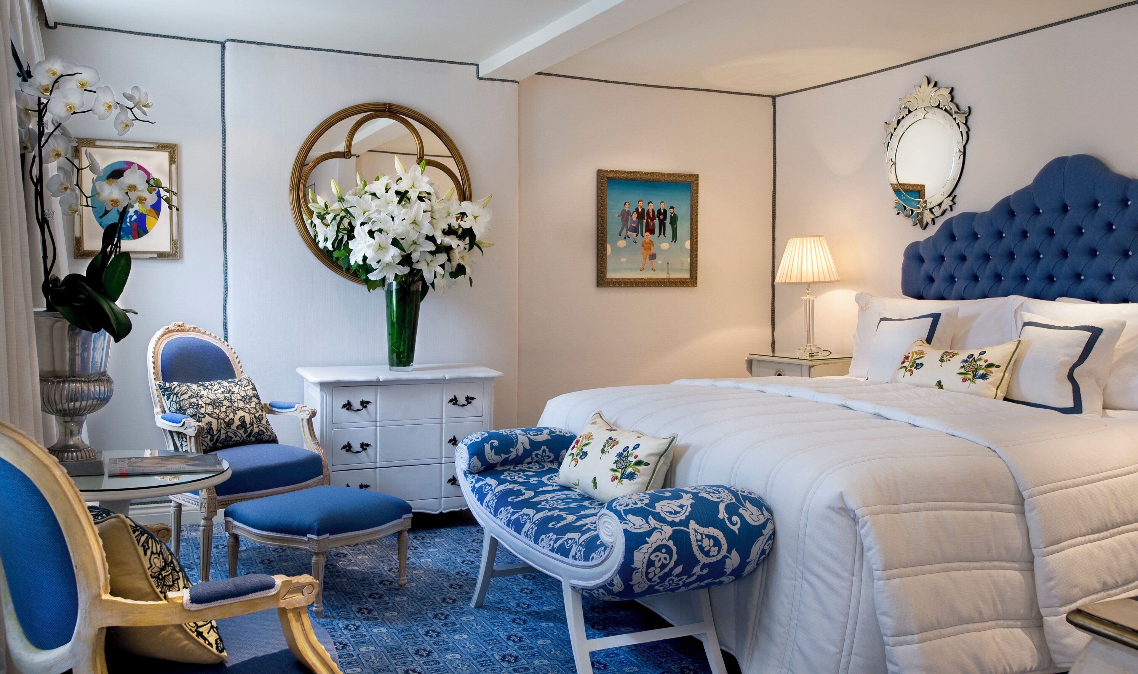 A bedroom with a large bed, a chair, a dresser, a mirror, and a painting on the wall.