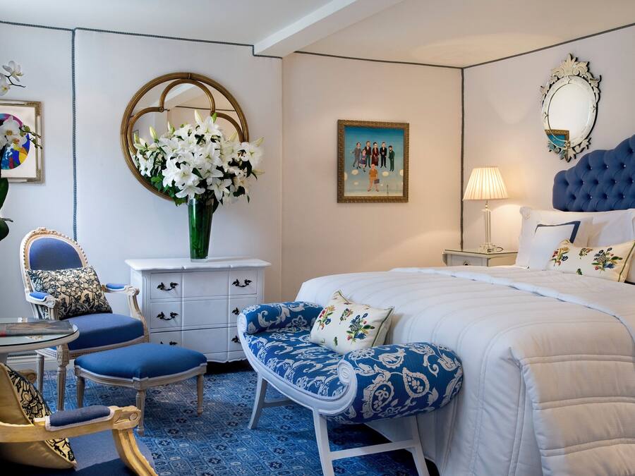 Um quarto com uma cama grande, uma cadeira, cômoda, espelho e um quadro na parede.