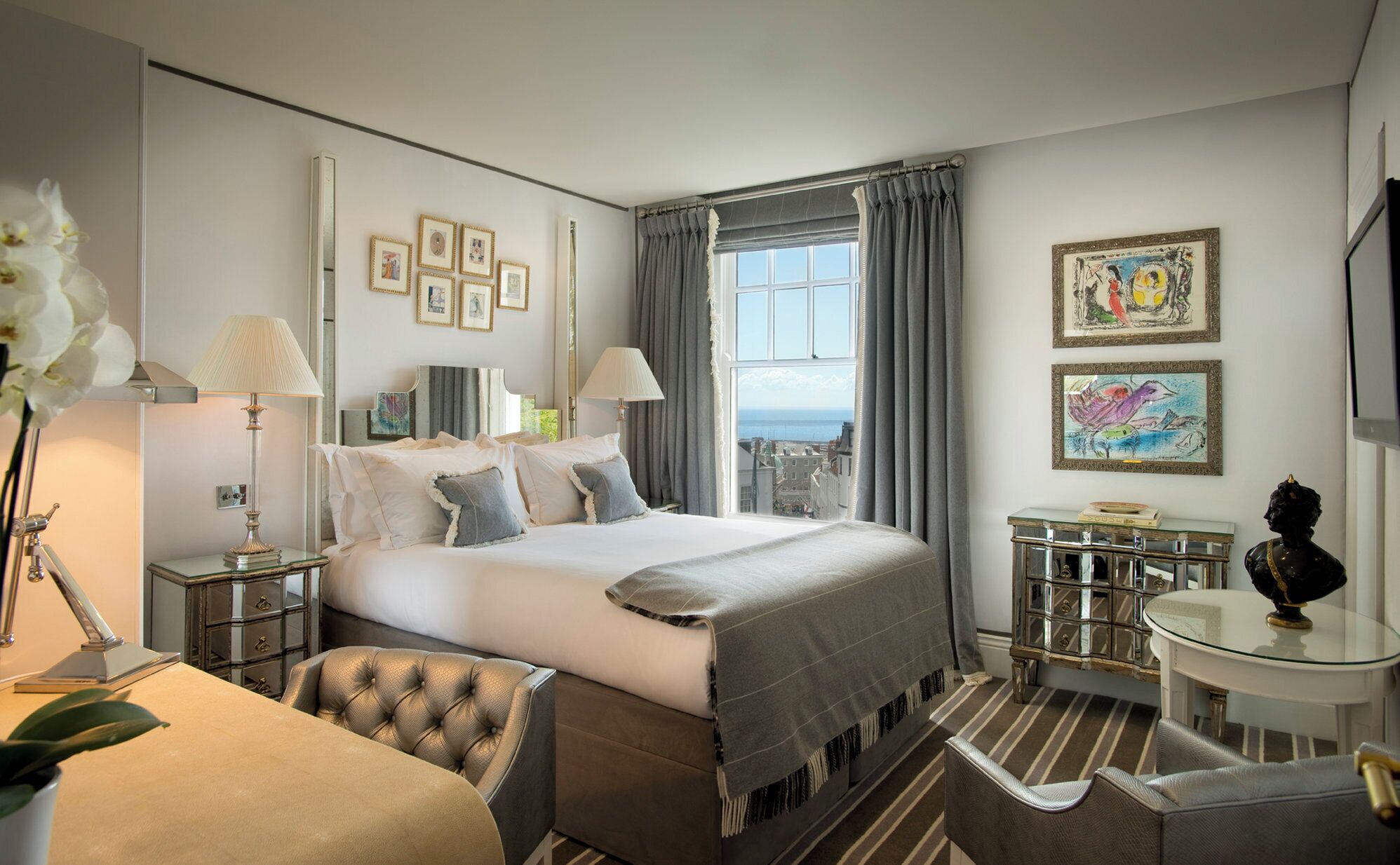 Une chambre d’hôtel équipée d’un lit, de tables de chevet, d’un bureau, d’une chaise et d’œuvres d’art accrochées aux murs.