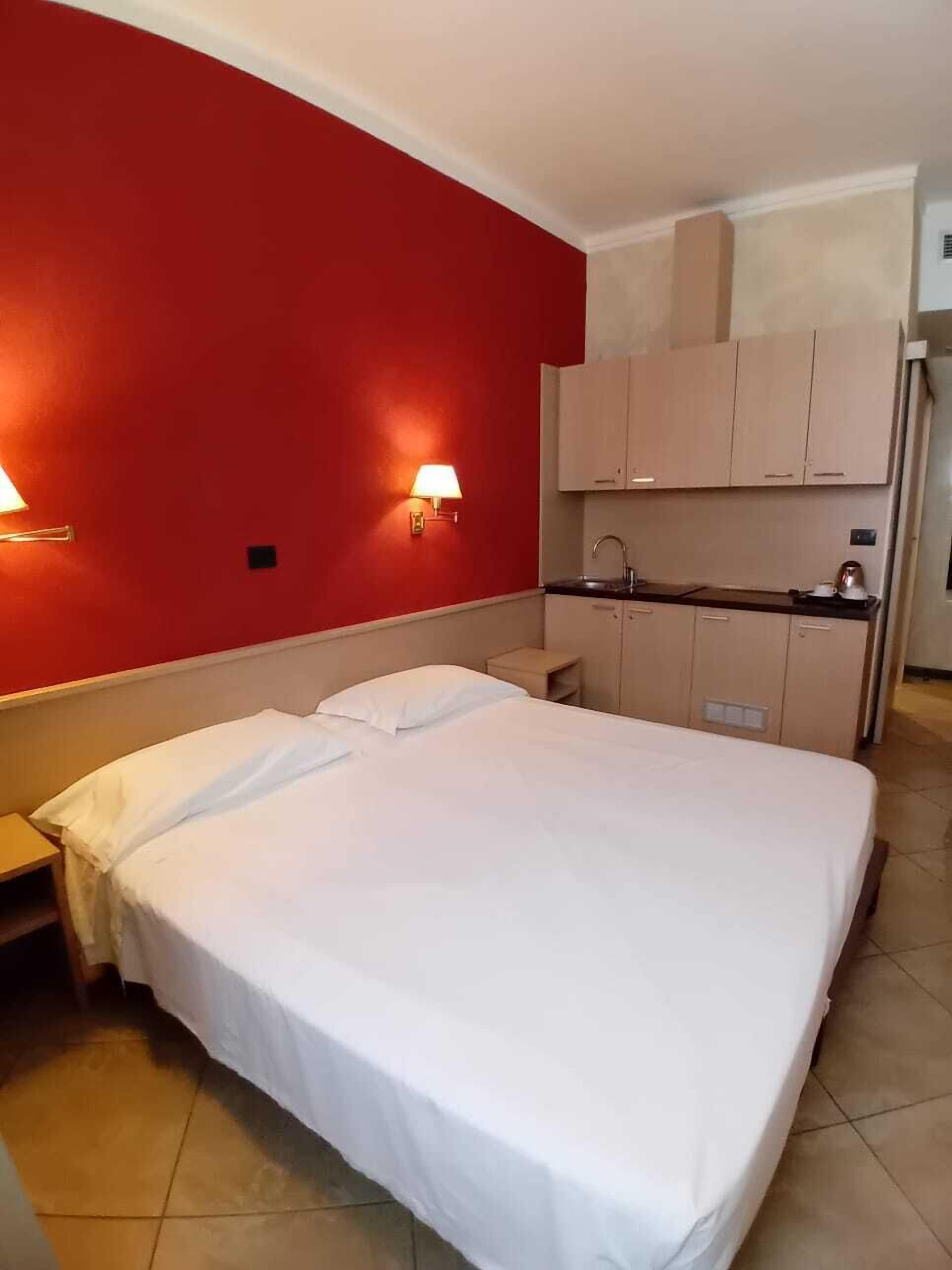 Una habitación de hotel con cama, una kitchenette pequeña y una pared roja decorativa.