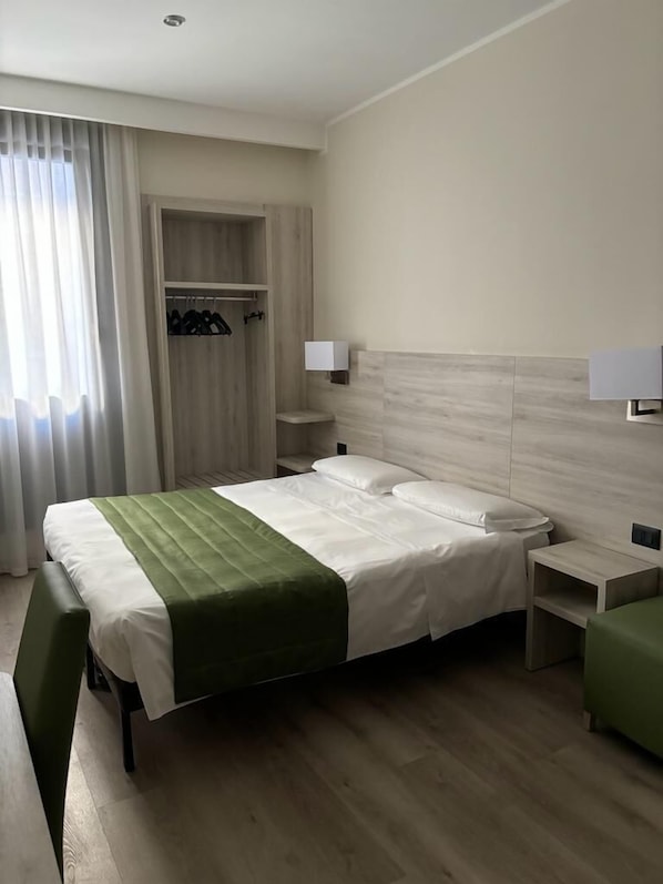 Una habitación de hotel con una cama, un banco, un armario y una mesita de noche.