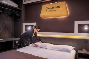Une chambre d’hôtel avec un lit, une table de chevet, une étagère fixée au mur et une pancarte indiquant « Gianduotto Torino ».