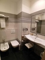A bathroom with a bidet, toilet, sink, and mirror.