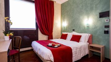 A hotel room with a bed, a desk, a chair, a window with red curtains, and a green wall.