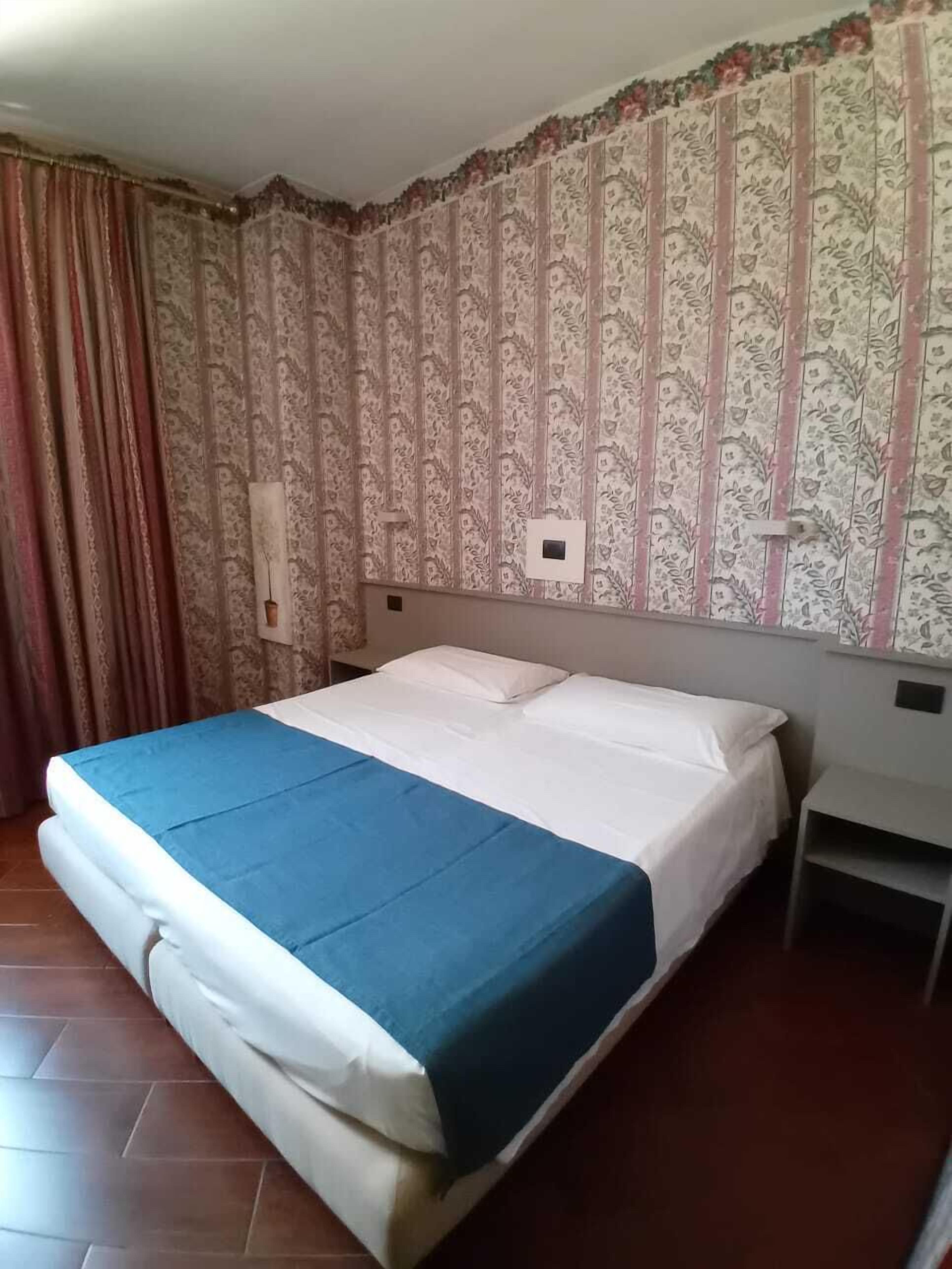 A single-bed room with a patterned wallpaper, a blue bedspread, and a curtain on the left.