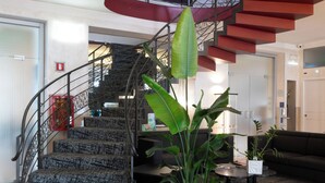 A modern interior with a spiral staircase, a living area with a sofa, and potted plants. - Hotel Plaza Torino (Turin)