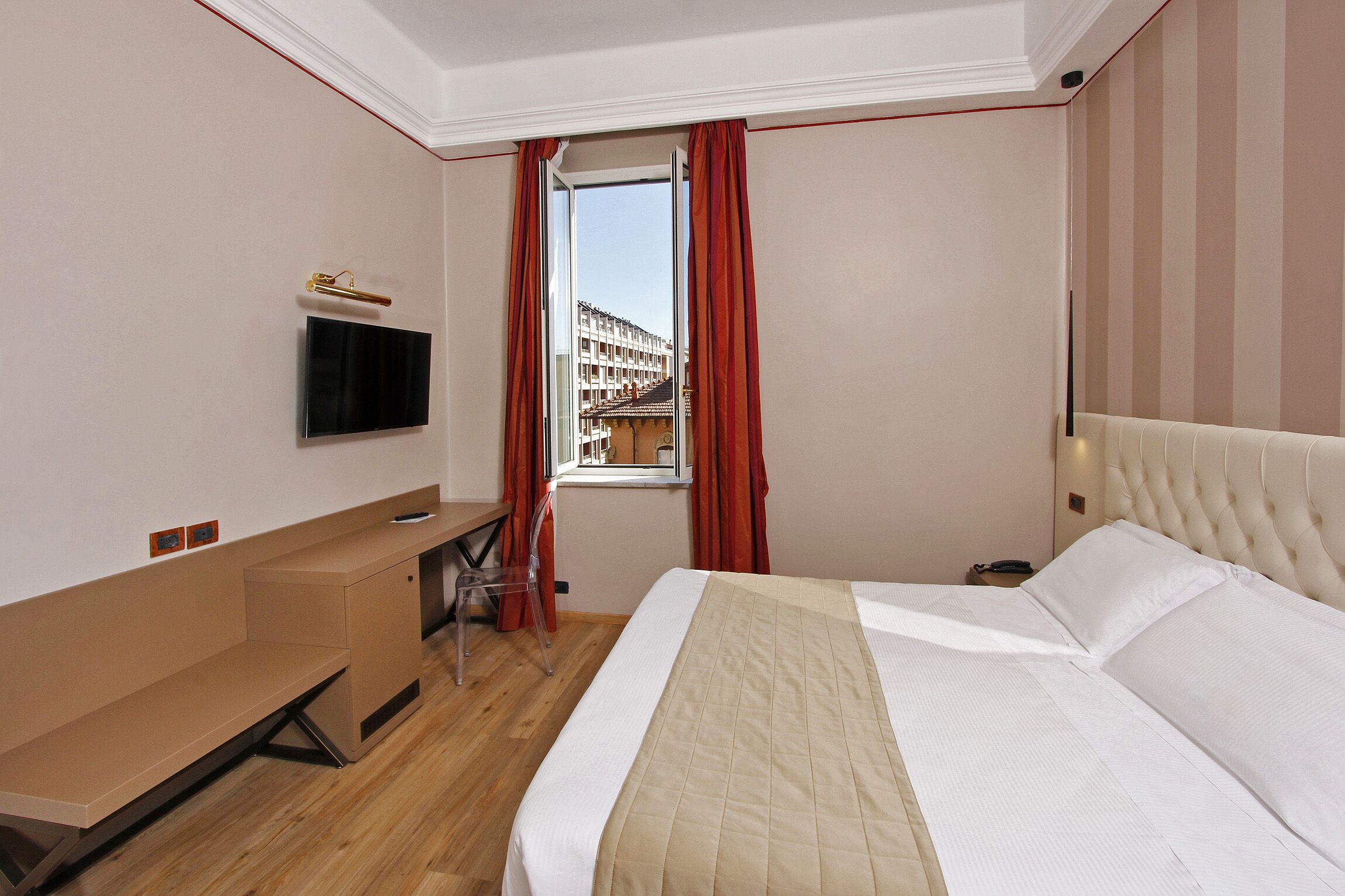 Una habitación de hotel con cama, escritorio, televisor y ventana con cortinas.