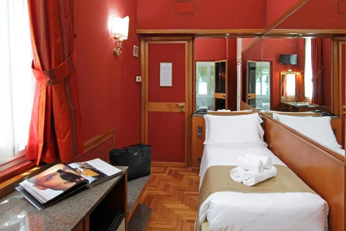 Una habitación de hotel con cama, escritorio, revista, maleta, espejo y puerta.