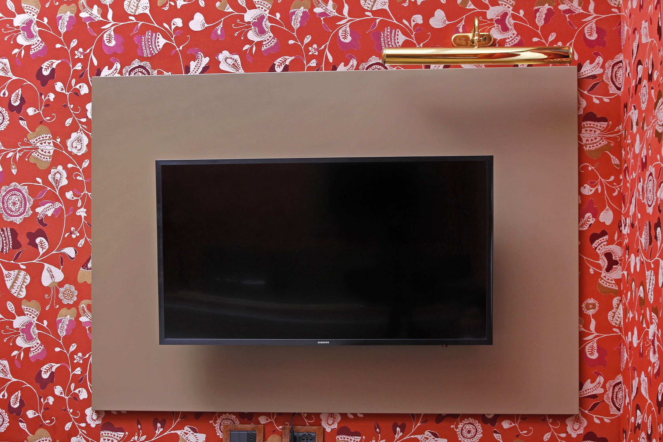 A flat-screen TV mounted on a wall with a floral wallpaper pattern.