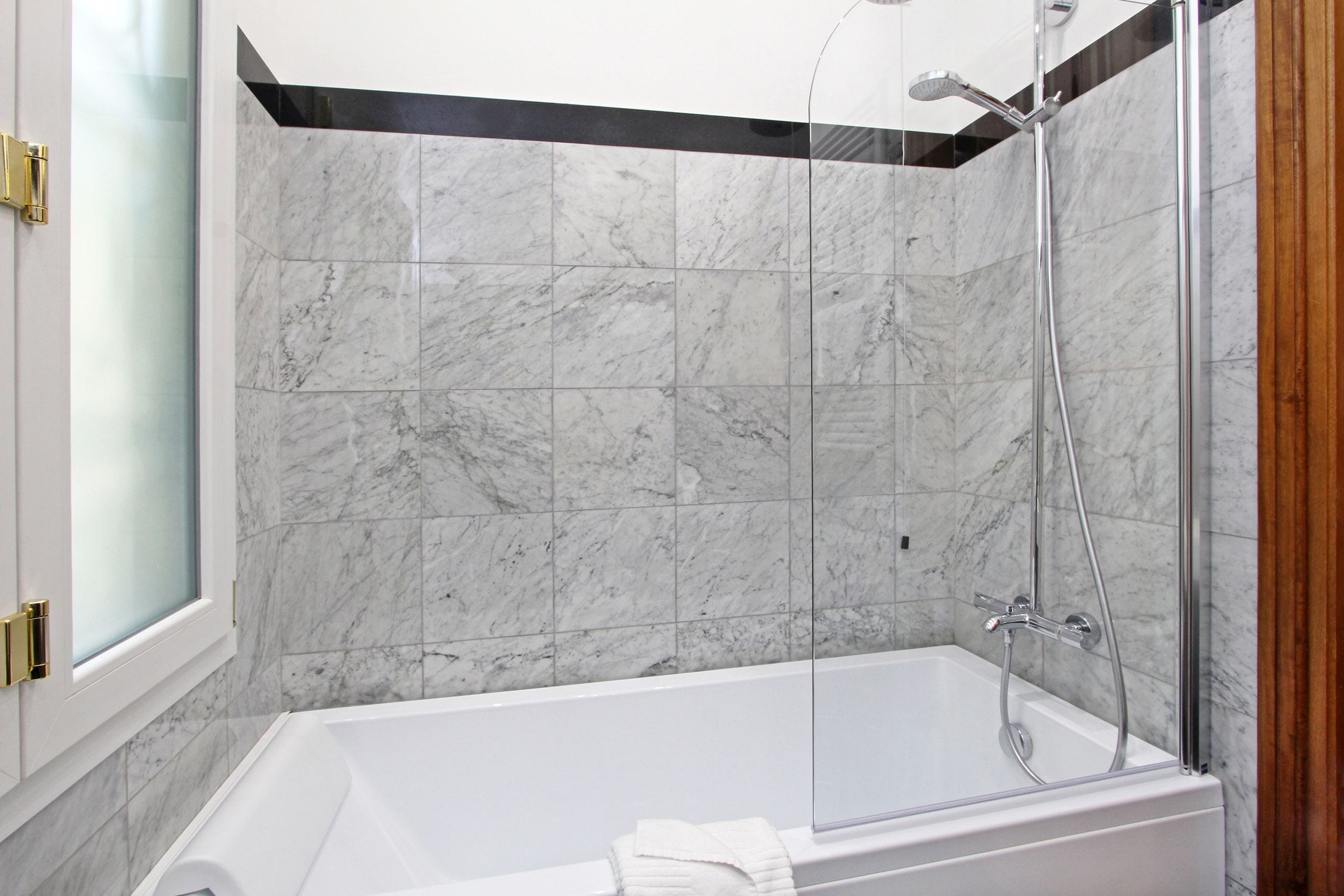 A modern bathroom with a glass-enclosed shower, a white bathtub, and marble tiles.