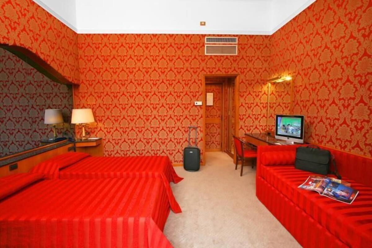 Habitación de hotel con dos camas, un escritorio con computadora, una silla, una maleta y una revista en el sofá.