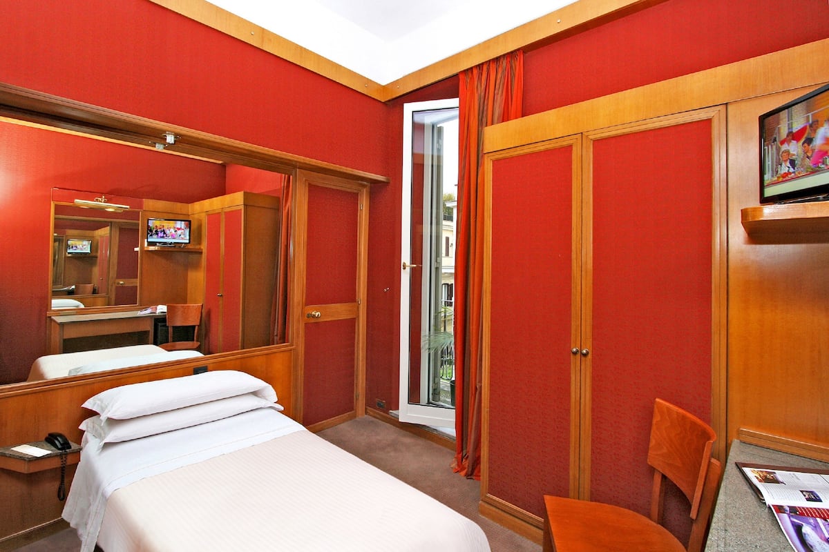 Habitación de hotel con una cama, un escritorio con teléfono, una silla, un televisor y un ventanal corredero que da a un área exterior.