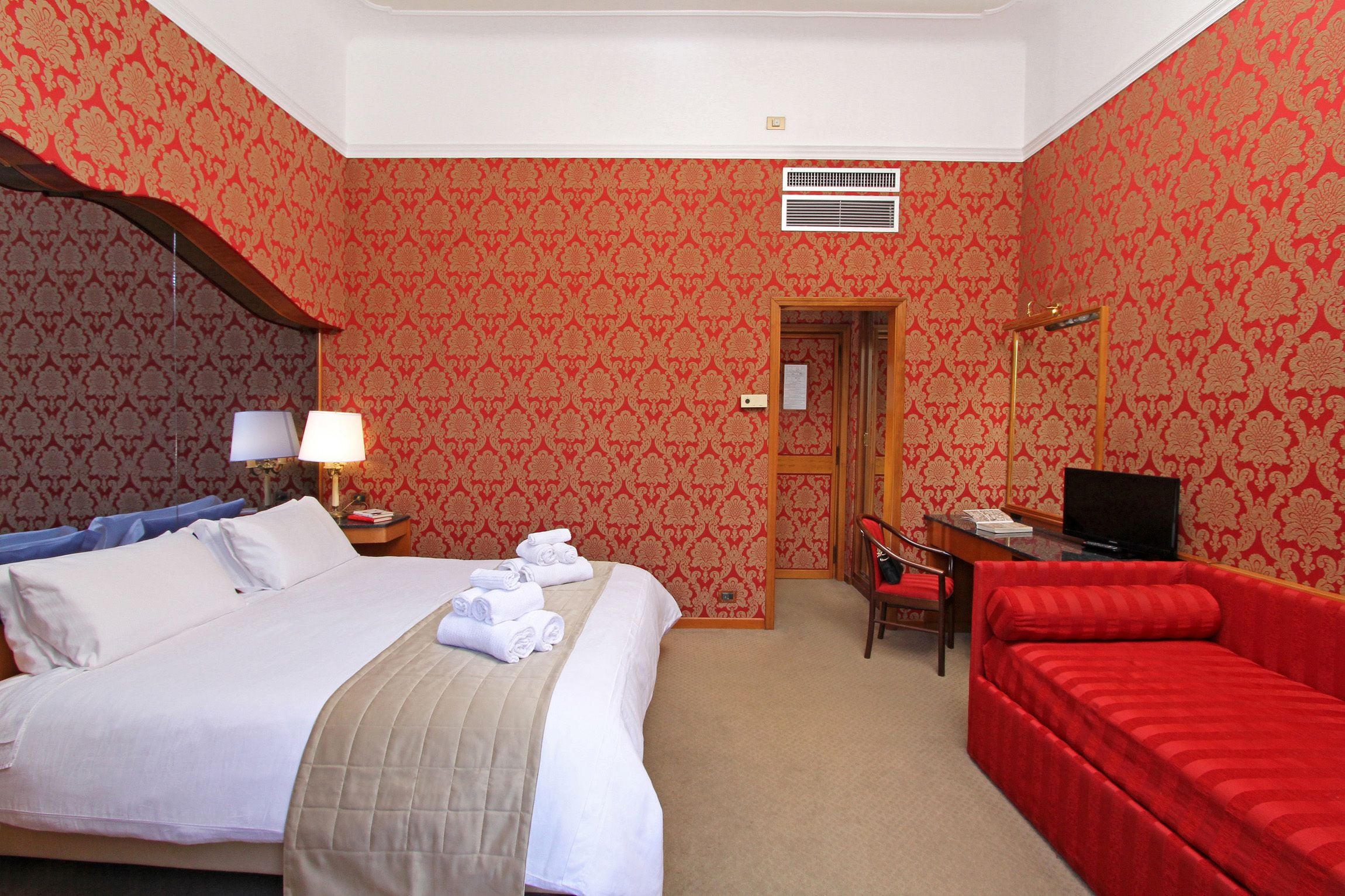A hotel room with a bed, a desk, a chair, and a red sofa.