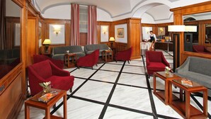 Een hotel lobby met een marmeren vloer, rode en grijze banken, houten meubels en een bar.