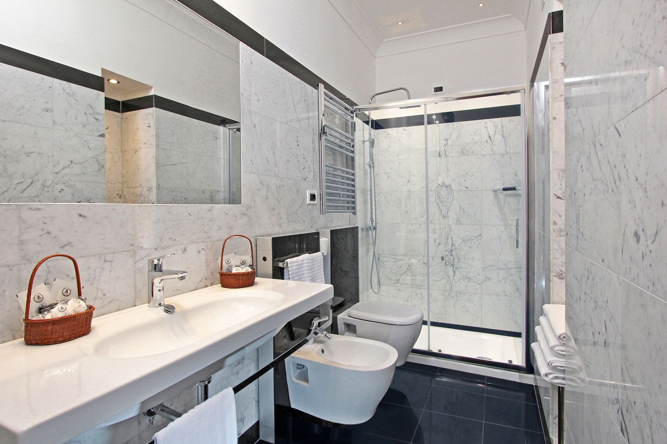 Un baño moderno con un espejo grande, dos lavamanos, un bidé y una ducha con cerramiento de vidrio.