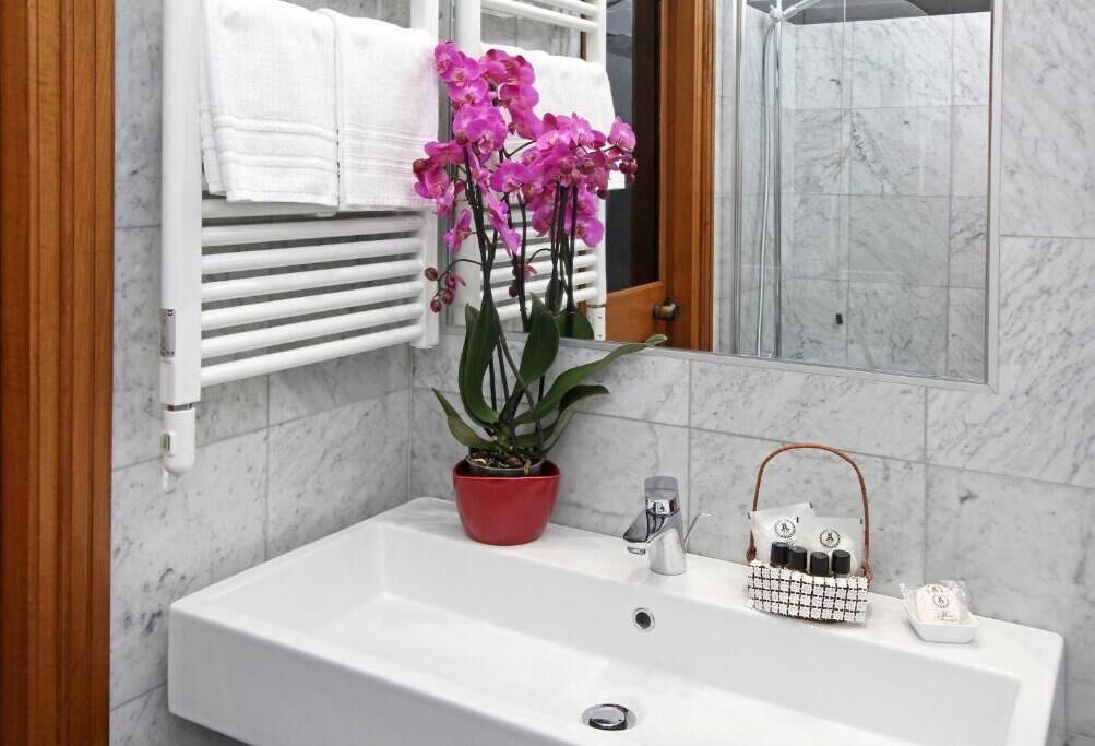 A bathroom with a white sink, a red potted plant, a white towel rack, and a mirror reflecting a shower area.
