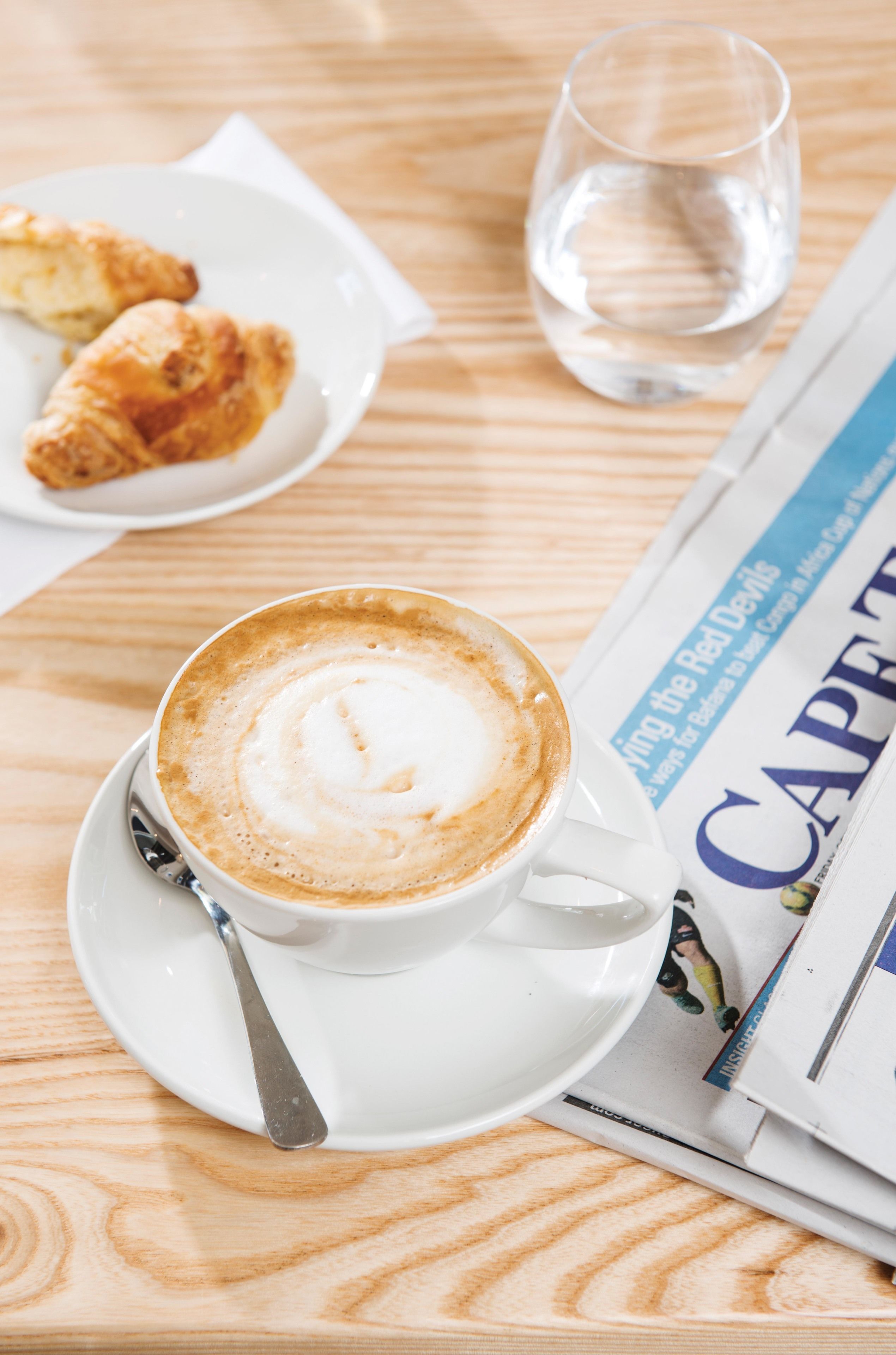 A table with a cup of coffee, a glass of water, and a plate of croissants.