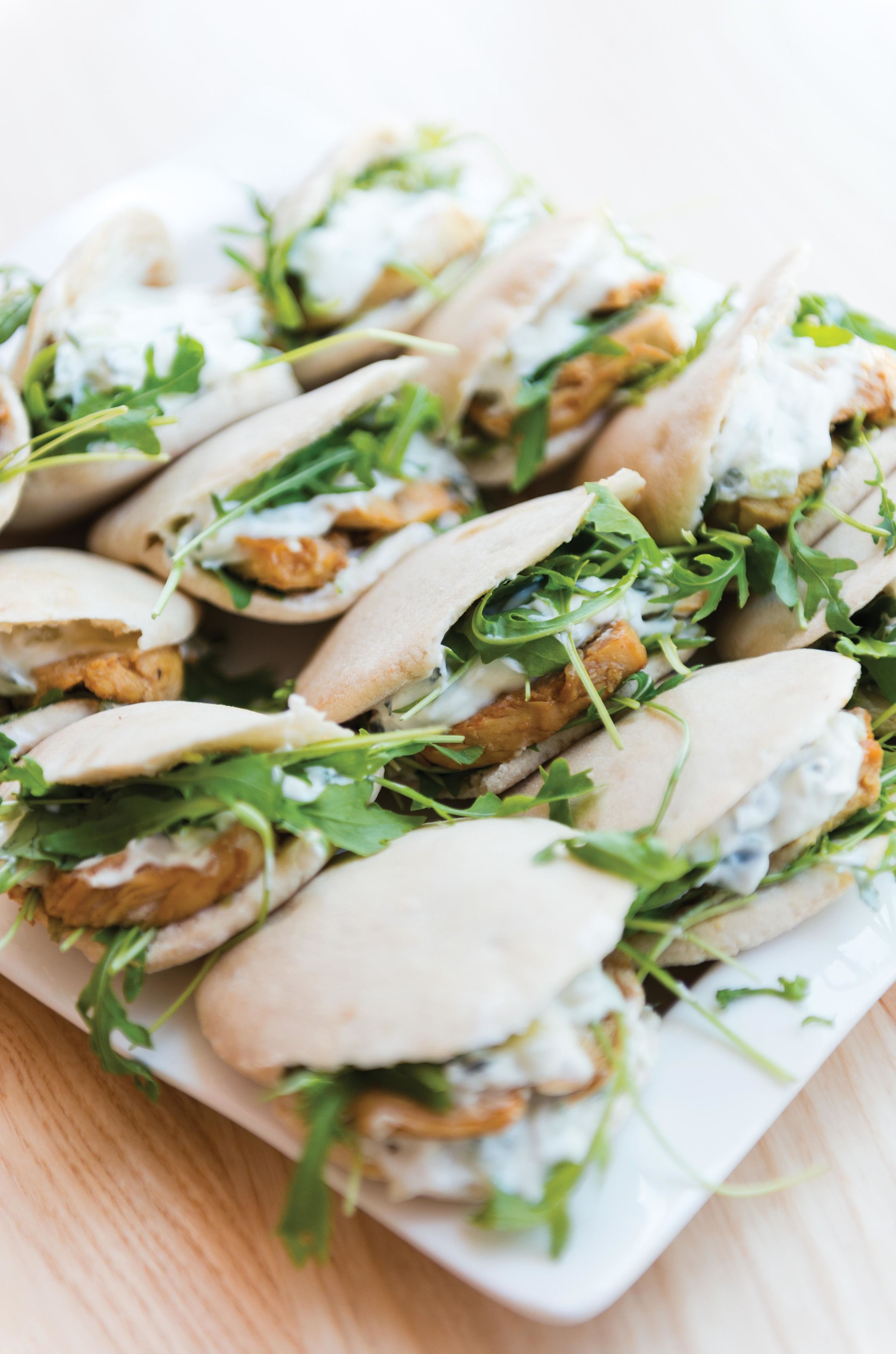 Un plato de sándwiches con hojas verdes frescas y salsa cremosa.