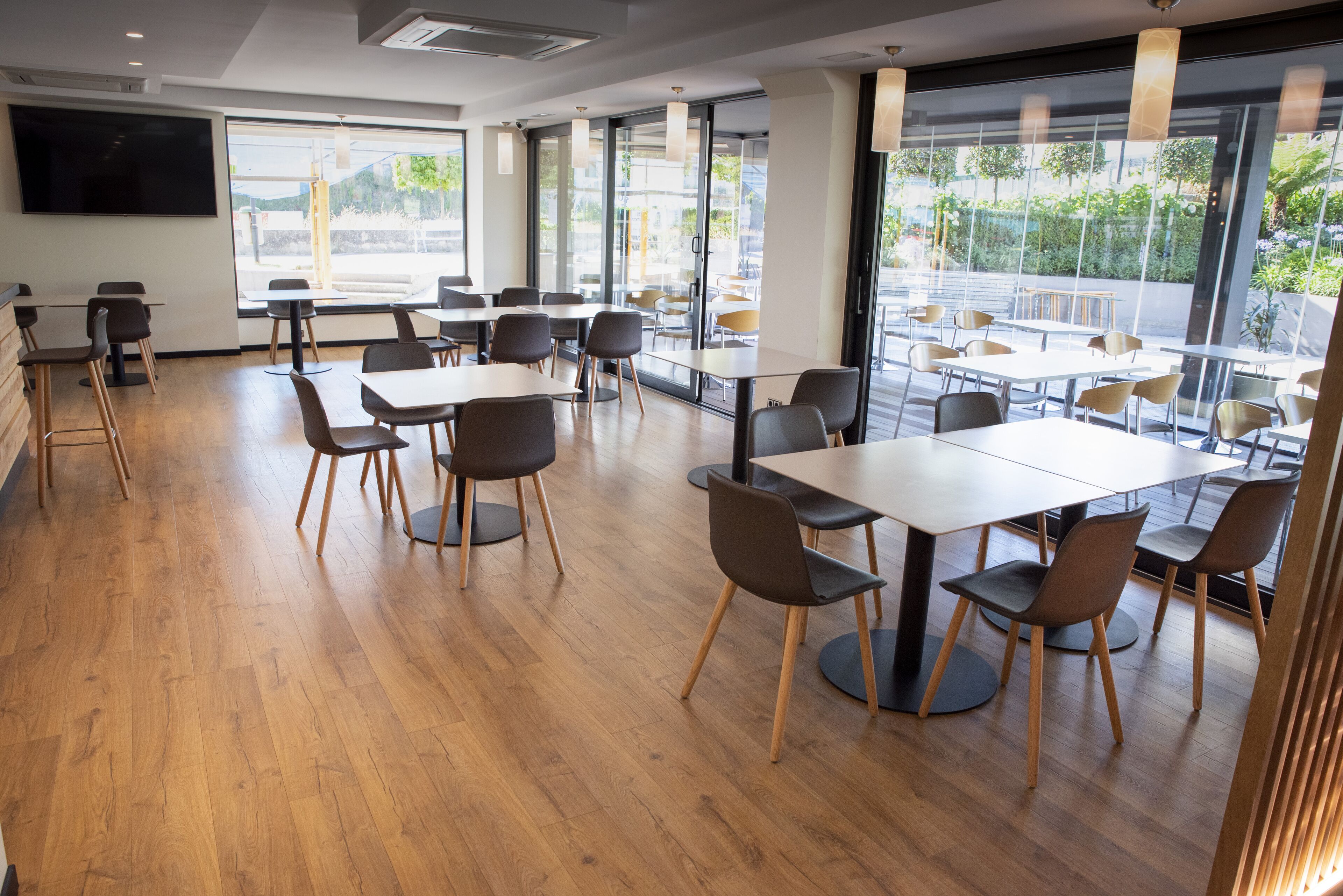 A modern dining area with wooden flooring, tables, and chairs arranged for groups.