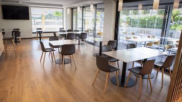 A modern dining area with wooden flooring, tables, and chairs arranged for groups.