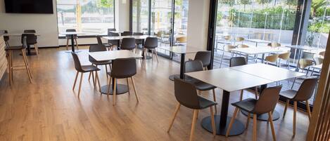 A modern dining area with wooden flooring, tables, and chairs arranged for groups.