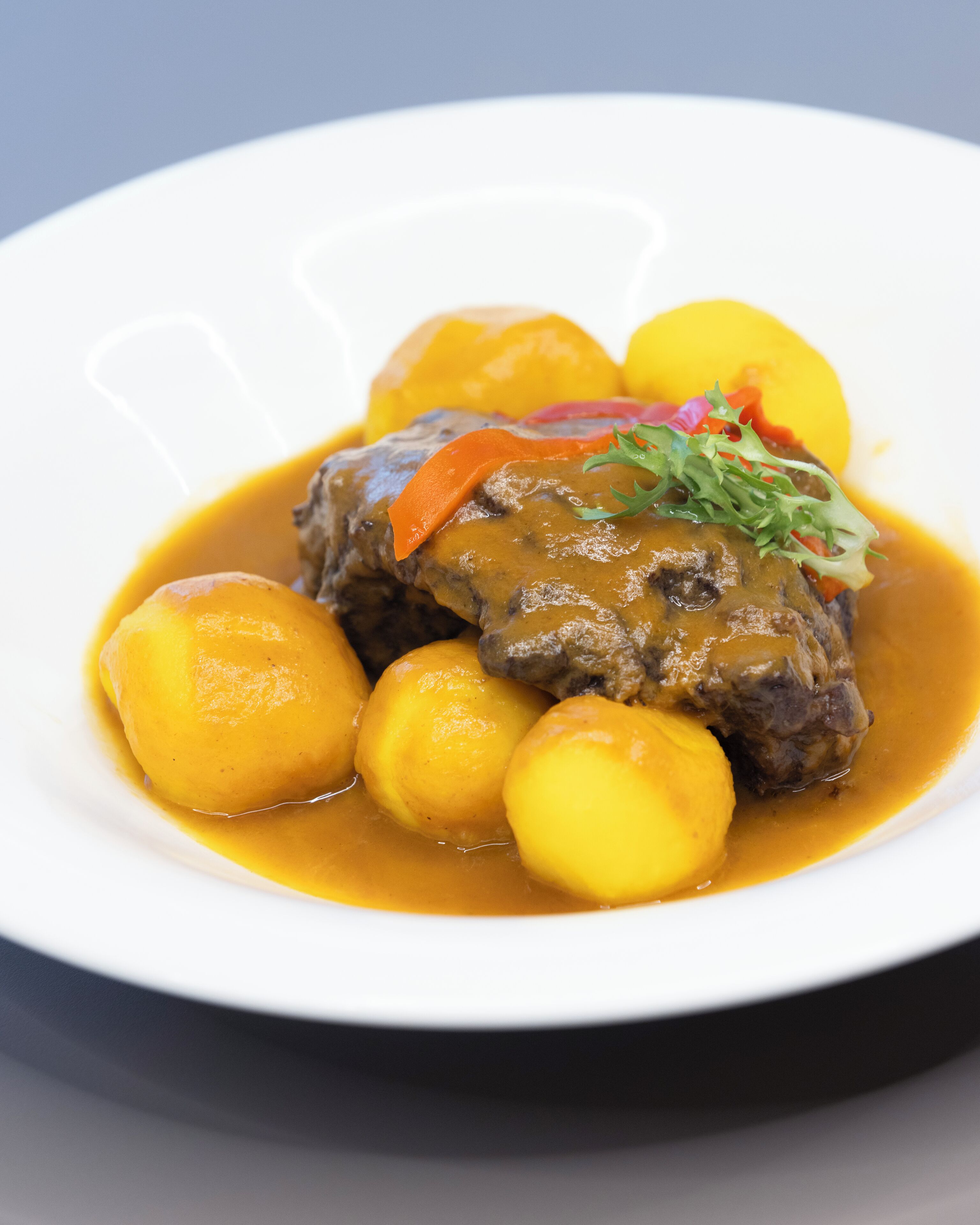 Une assiette de bœuf nappé de sauce et accompagnée de pommes de terre bouillies.