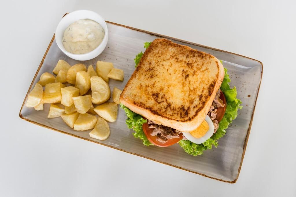 Un sándwich con lechuga, tomate y huevo sobre pan tostado, acompañado de papas a la francesa y un recipiente pequeño con salsa.