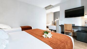A hotel room with a bed, a desk, a chair, a television, and a small kitchenette.