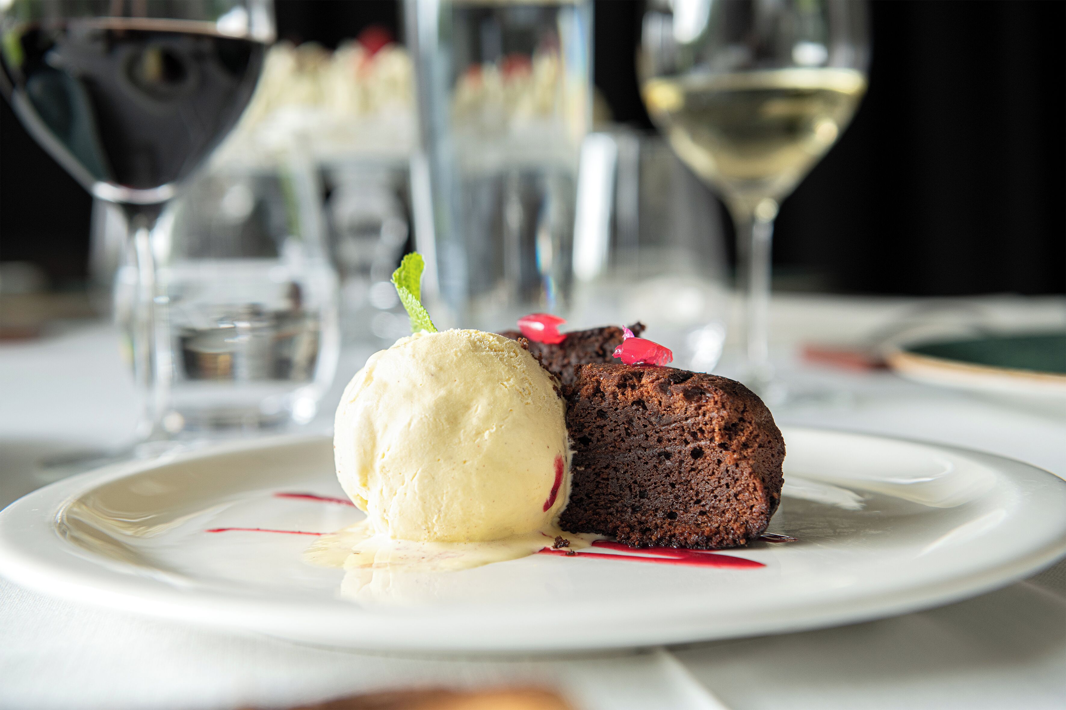 Dessert auf einem weißen Teller, im Hintergrund ein Glas Weißwein.
