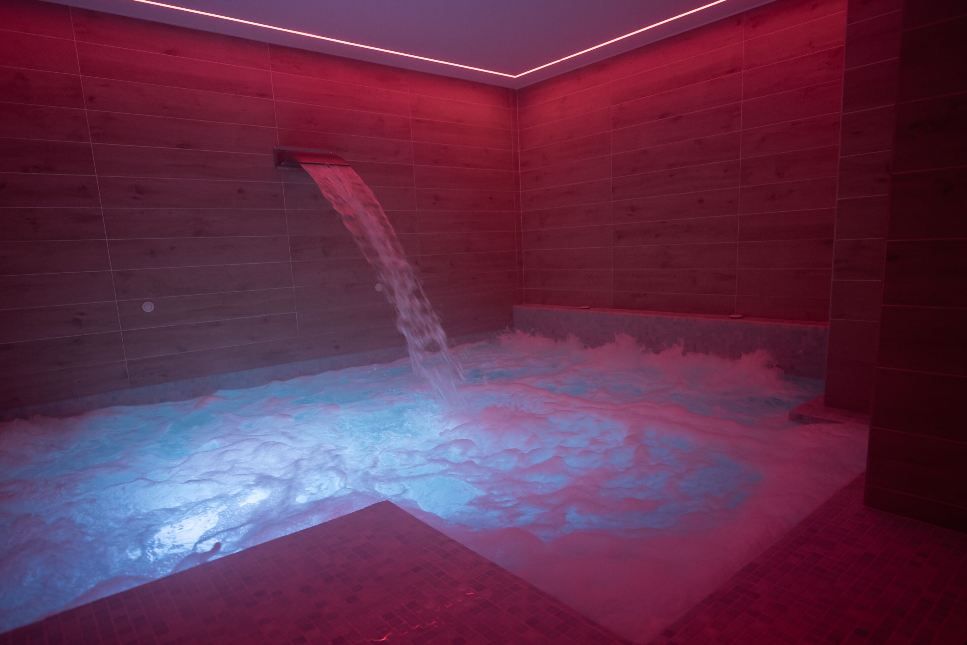 A room with a red-lit wall, a water feature, and a tiled floor.