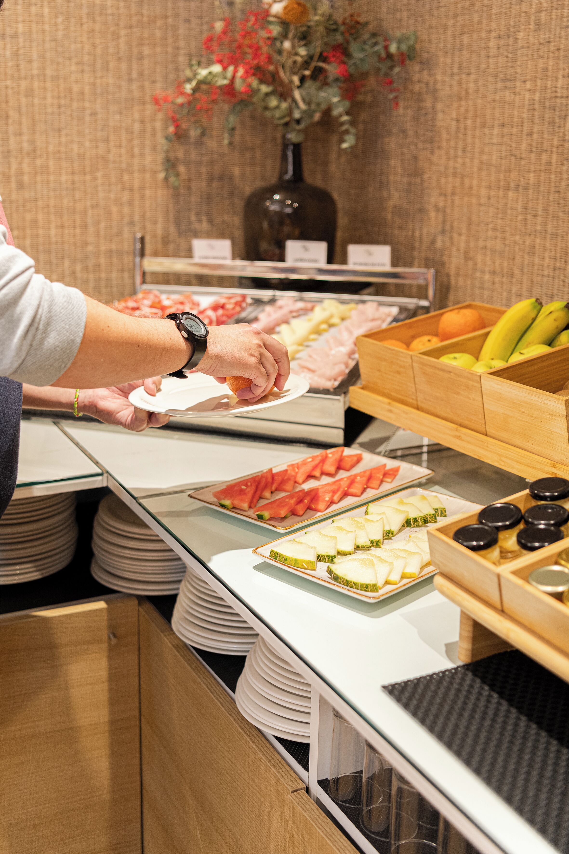 A buffet setup with various food items and a person serving themselves.