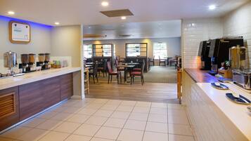 Un comedor de hotel con una barra de buffet, mesas y sillas, y una estación de café.