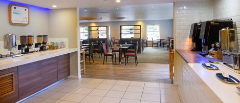 A hotel dining area with a buffet counter, seating arrangements, and a coffee station.