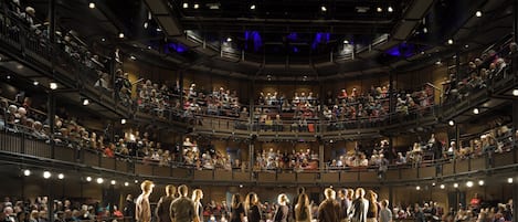 Un amplio auditorio interior con varios niveles de butacas, un escenario central y una multitud de personas.
