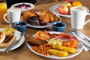 A breakfast table with various food items including toast, muffins, croissants, bacon, eggs, beans, sausages, and fruit. - Holiday Inn Express Warwick - Stratford-upon-Avon by IHG (Warwick)