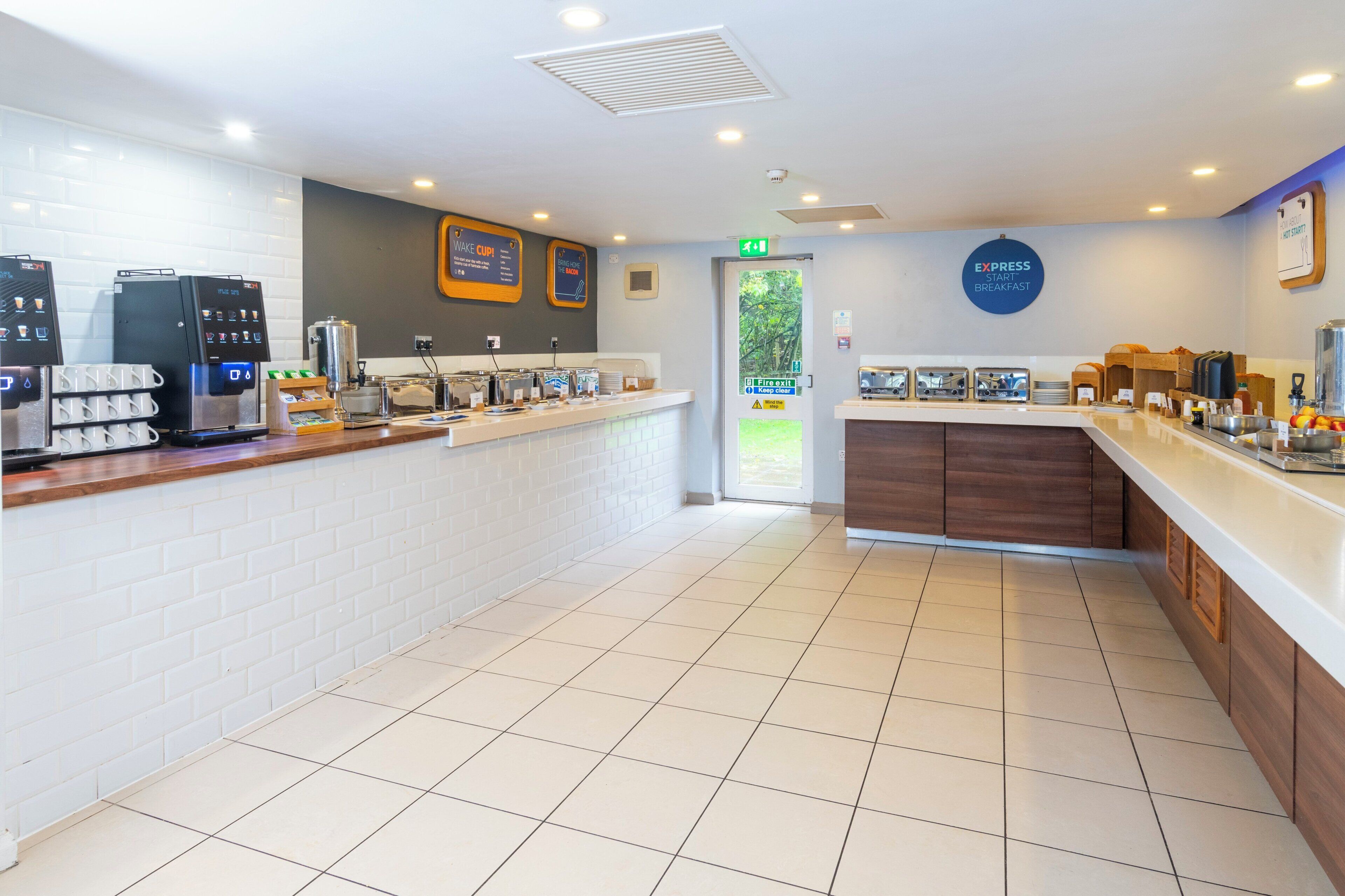 A modern breakfast area with a coffee machine, tea station, and a sign for 'EXPRESS START BREAKFAST'.