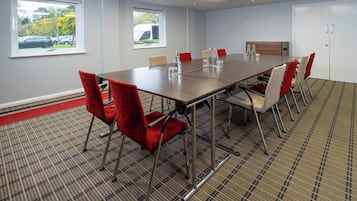 A conference room with a long table, red and beige chairs, and a patterned carpet.