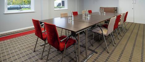 Une salle de conférence avec une longue table, des chaises rouges et beiges, et un tapis à motifs.