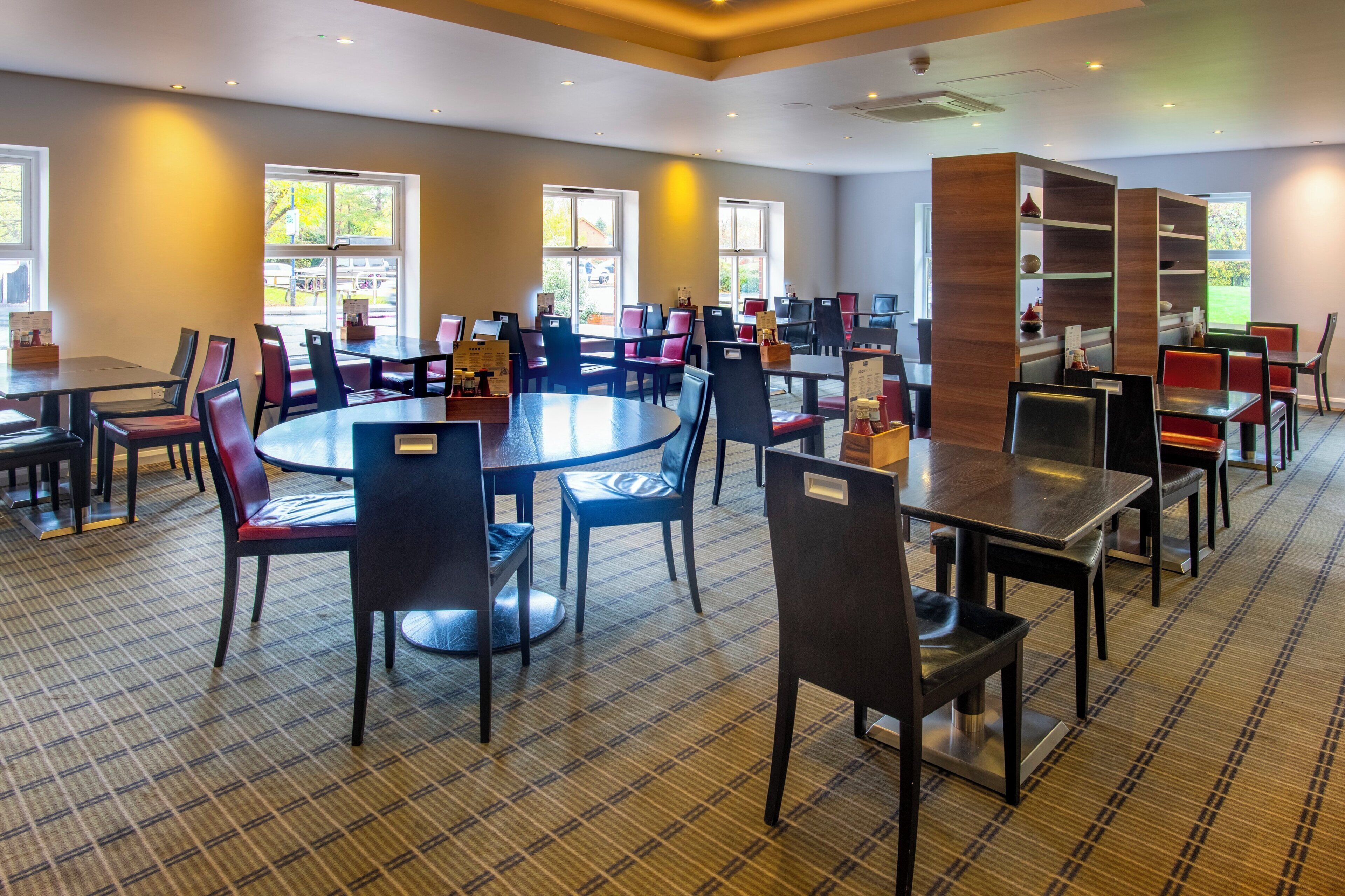 A spacious dining area with multiple tables and chairs, large windows providing natural light, and a check-in counter.
