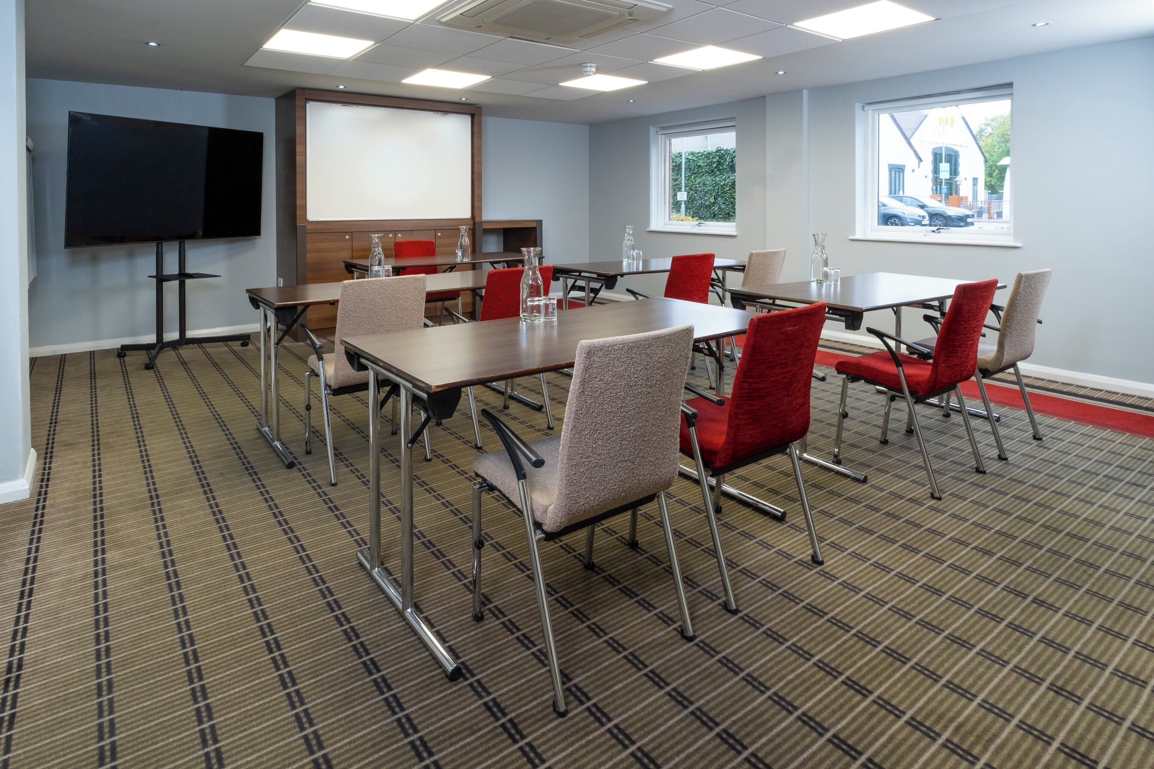 Une salle de conférence avec une grande table, des chaises rouges, un tableau blanc et un écran de télévision.