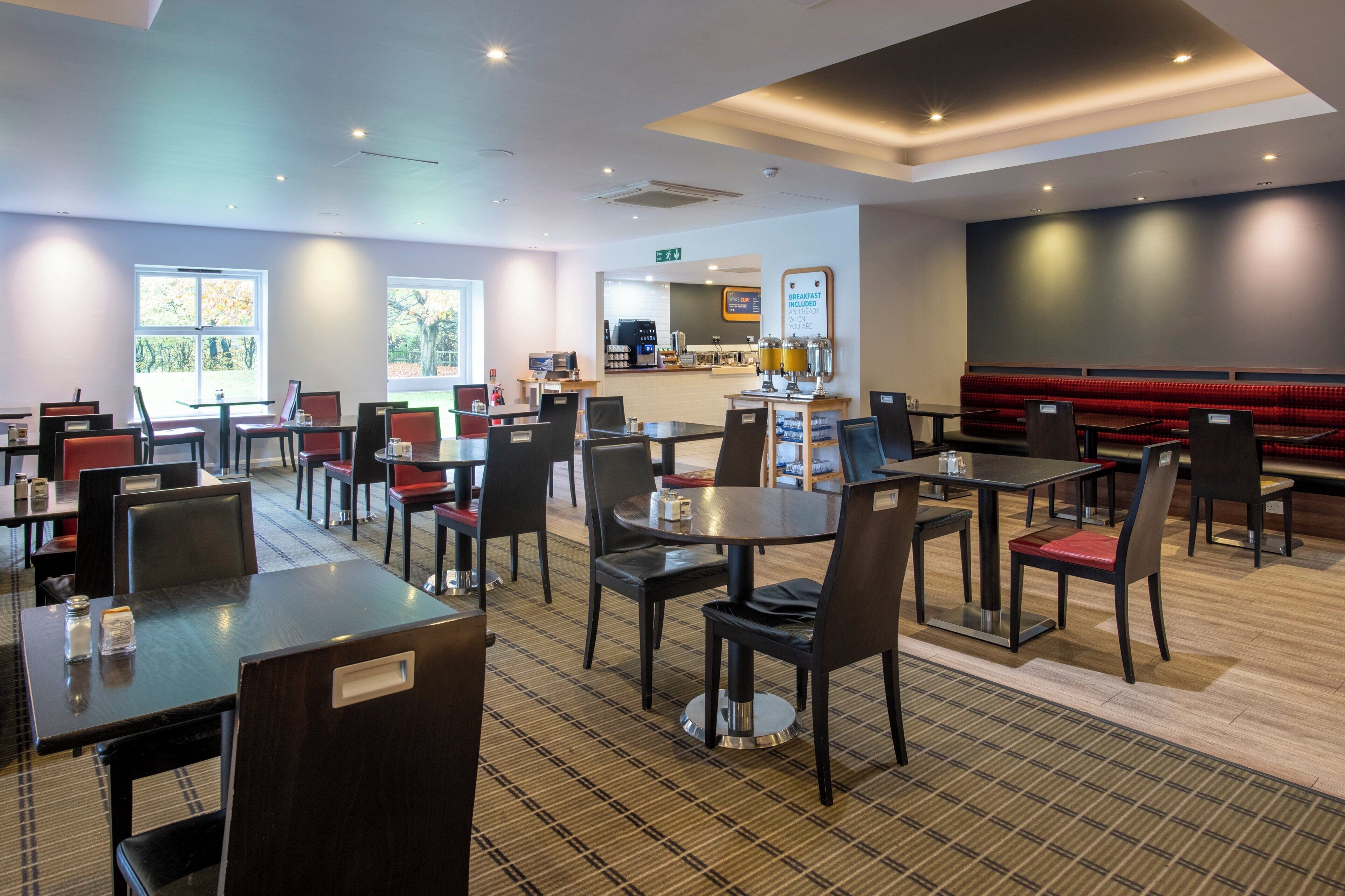 A modern restaurant with multiple tables and chairs, a coffee bar, and a red cushioned seating area.